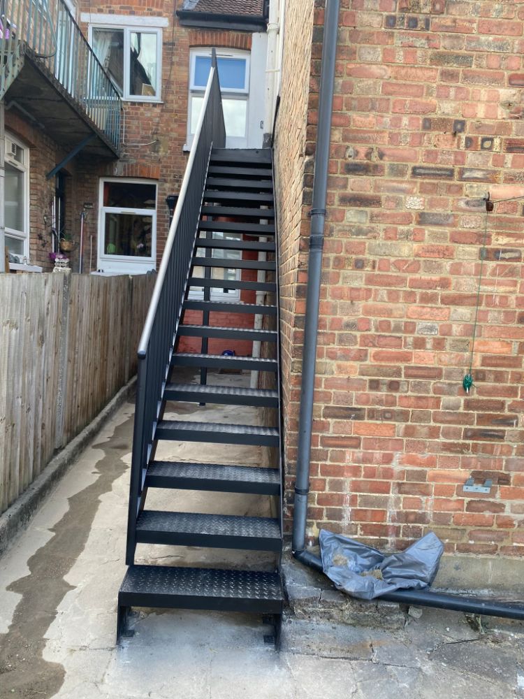 Straight external staircase with black metal frame against brick building