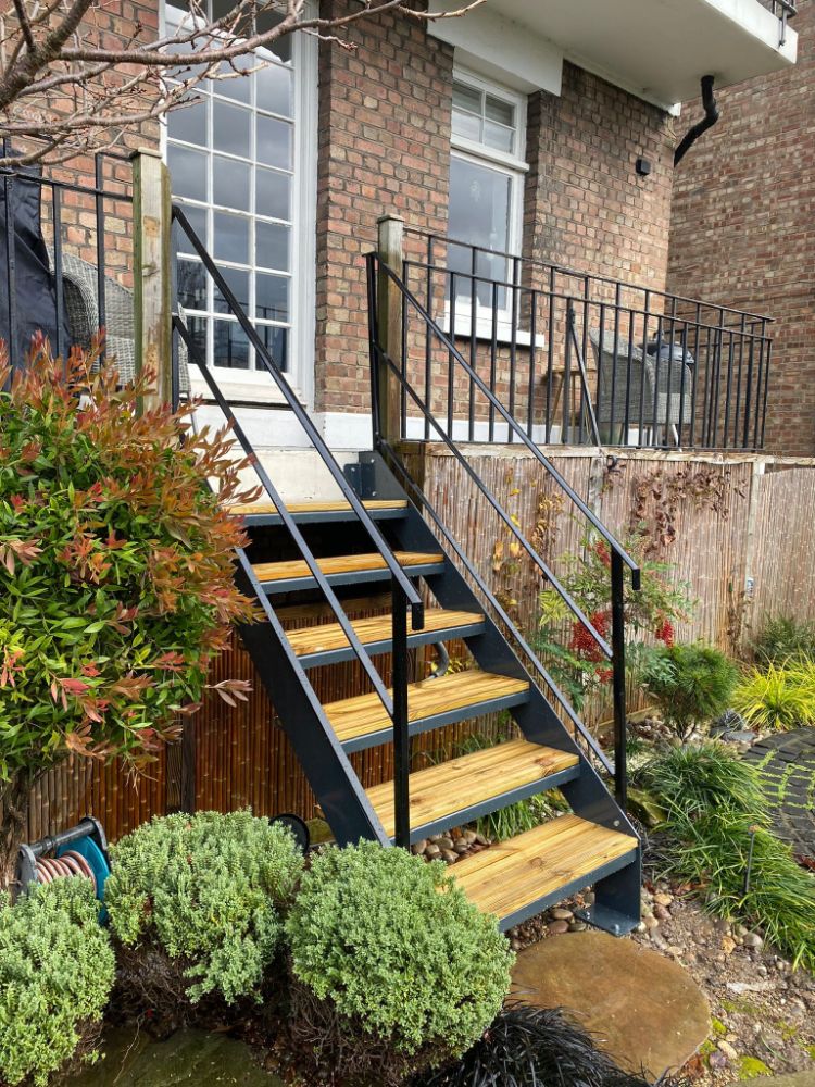 Elegant external staircase with wooden treads and black metal frame through garden