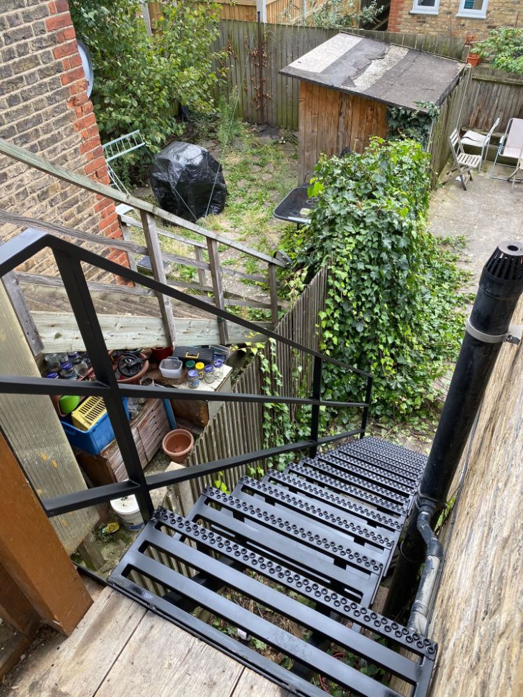 Black metal staircase with perforated treads descending to garden area