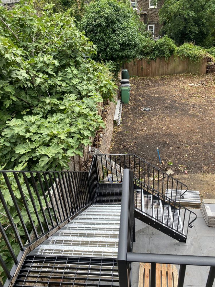 Multi-level black metal staircase with complex angular design in courtyard